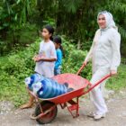 Bunda PAUD Aceh, Marlina Muzakir, membantu Cut Shofi membawa kereta Sorong bermuatan dua galon air yang di angkut dari sungai, di Gampong Pante Bahagia Kecamatan Paya Bakong Kab. Aceh Utara, Selasa (14/10/2025). dok. Ist