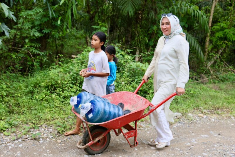Bunda PAUD Aceh, Marlina Muzakir, membantu Cut Shofi membawa kereta Sorong bermuatan dua galon air yang di angkut dari sungai, di Gampong Pante Bahagia Kecamatan Paya Bakong Kab. Aceh Utara, Selasa (14/10/2025). dok. Ist