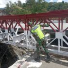 Ket foto : Babinsa Koramil 02/WPS melakukan pengecekan kondisi rangka dan baut pengunci Jembatan Bailey di Desa Jamur Ujung.(Dok/Ist)