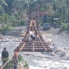 Personel Babinsa Posramil Lawe Sumur bersama teknisi lapangan dan masyarakat bergotong royong memasang papan lantai Jembatan Gantung Perintis di Desa Teger Miko, Kecamatan Lawe Sumur, Aceh Tenggara, Senin (6/7/2026). Foto: Dok. Istimewa 
