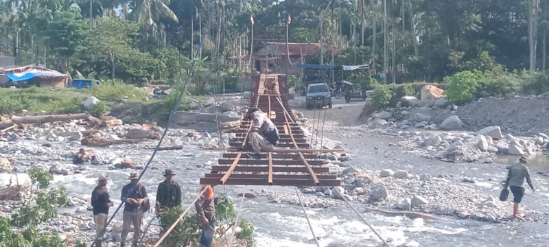 Personel Babinsa Posramil Lawe Sumur bersama teknisi lapangan dan masyarakat bergotong royong memasang papan lantai Jembatan Gantung Perintis di Desa Teger Miko, Kecamatan Lawe Sumur, Aceh Tenggara, Senin (6/7/2026). Foto: Dok. Istimewa 