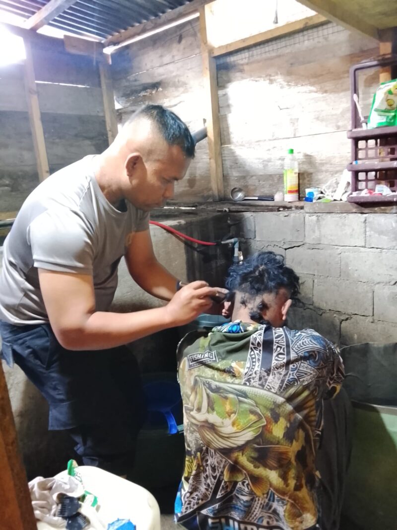 Aipda Candra Sugara, SH saat memangkas rambut pasien penderita gangguan saraf, Minggu (26/7/2026), di wilayah Kecamatan Bandar, Kabupaten Bener Meriah, sebagai bentuk kepedulian dan pelayanan humanis Polsek Bandar kepada masyarakat.(Dok: Rahmat Ramadhan/Acehnow.com)